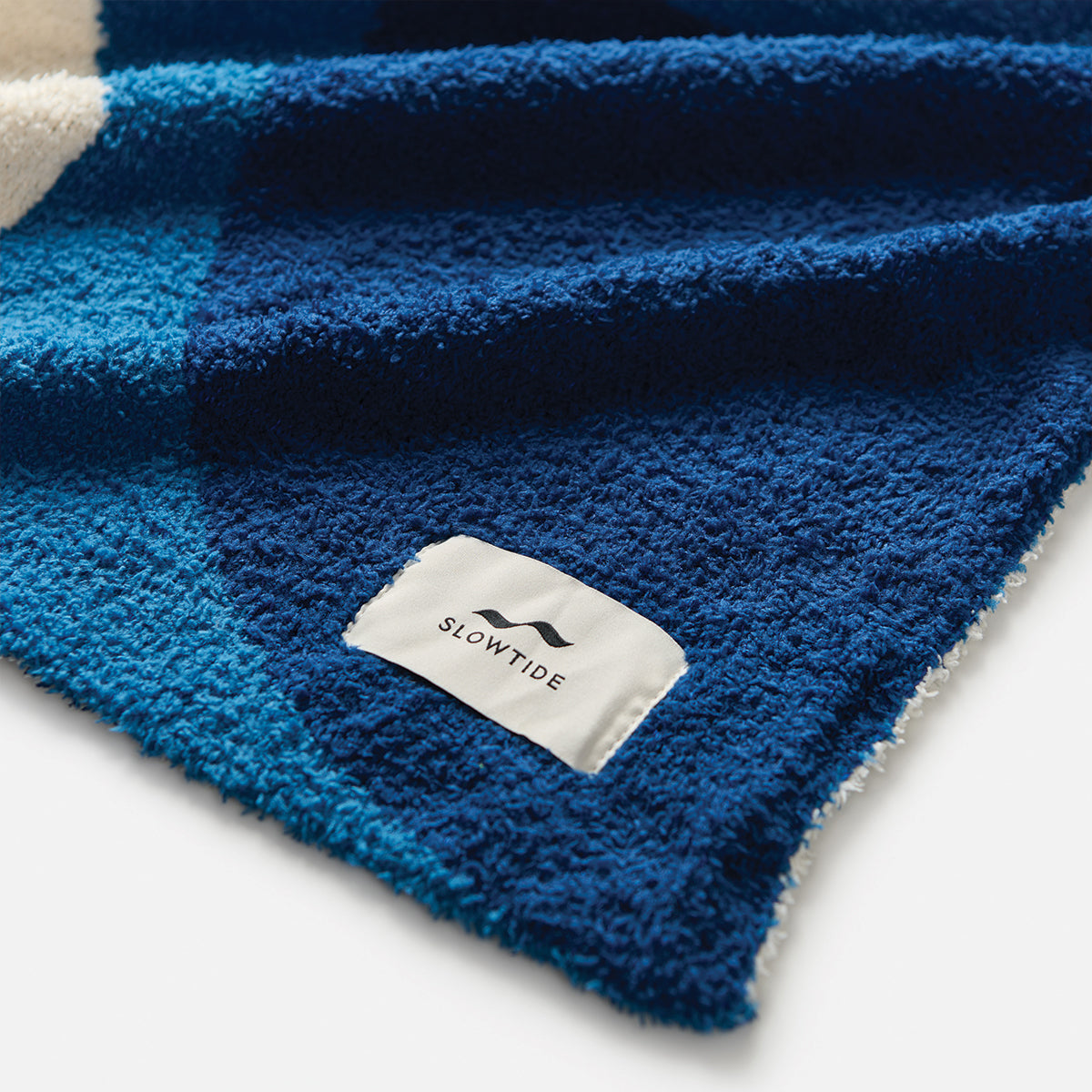 Plush blanket with blue and white pattern and woven logo patch.