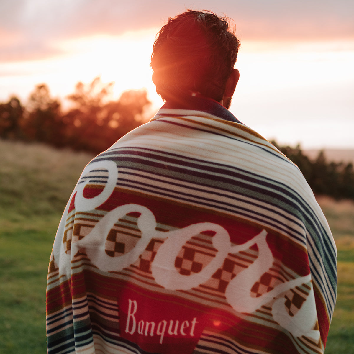 Plush blanket with logo design on grass at sunset.