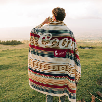 Recycled polyester blanket with a cozy wrap design shown outdoors on grass.