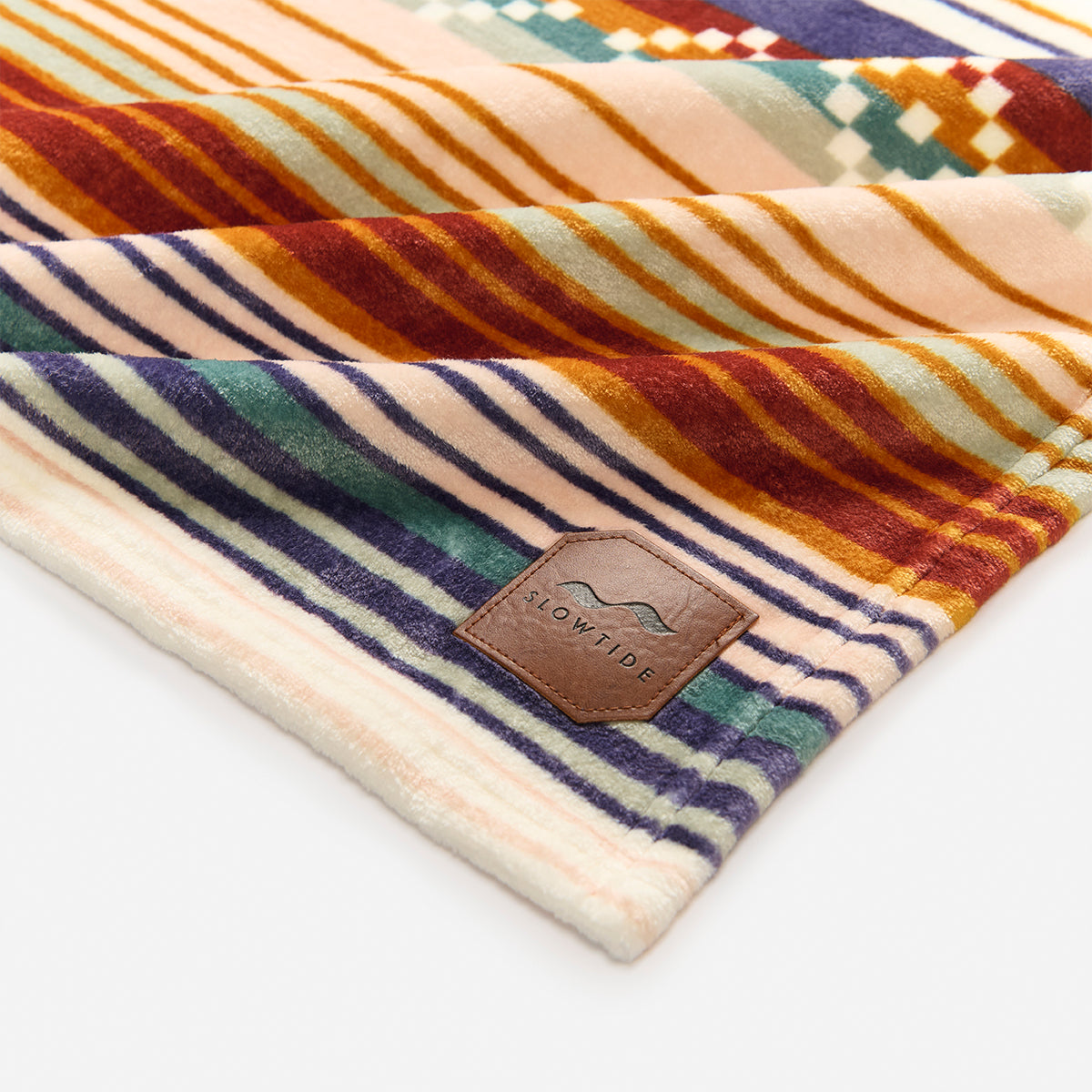 Plush blanket with colorful stripes and leather patch on a white surface.