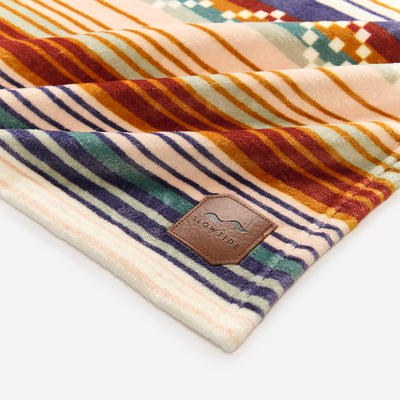 Plush blanket with colorful stripes and leather patch on a white surface.