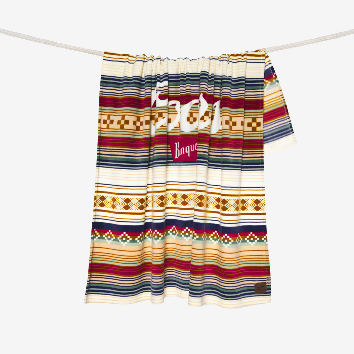 Recycled polyester blanket with colorful stripes and geometric patterns hanging on a line.