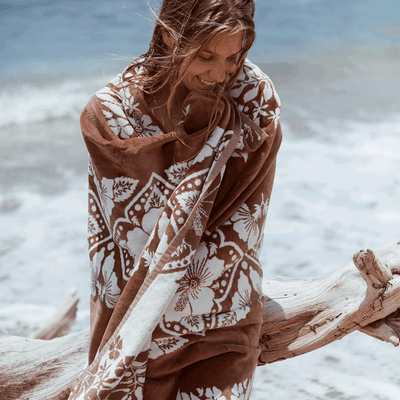 Cotton towel with floral pattern, absorbent, displayed on sandy beach by driftwood.