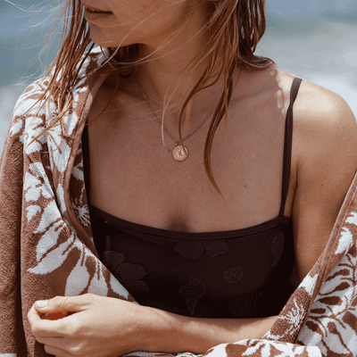Sustainable beach towel with gold necklace detail, shown at the beach.