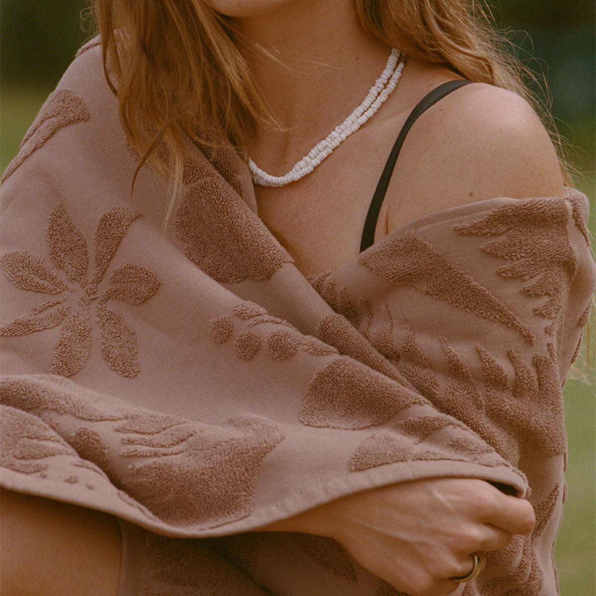 Beaded necklace and brown patterned beach towel in sustainably sourced cotton outdoors.