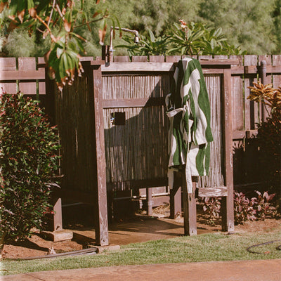 Outdoor shower with plush robe and green-striped towel on wooden fence.