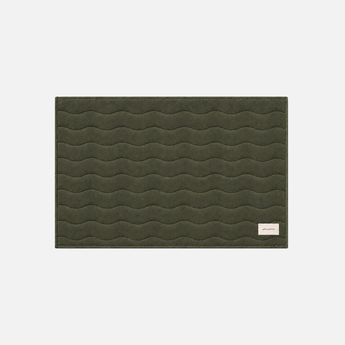 Cotton bath mat in dark green with wavy stitching and a beige tag in the corner.