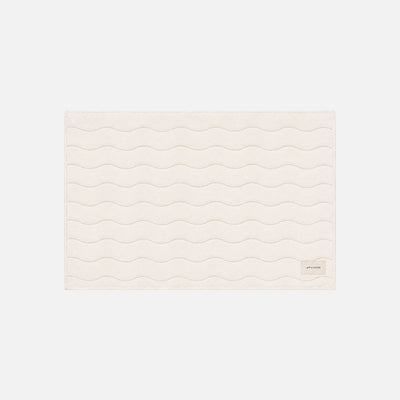 Beige cotton bath mat with wavy stitched lines and small bottom right label.
