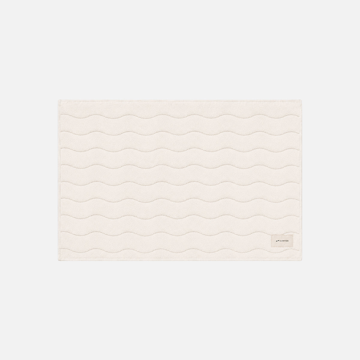 Cotton bath mat, cream, with wavy stitching and small corner tag.
