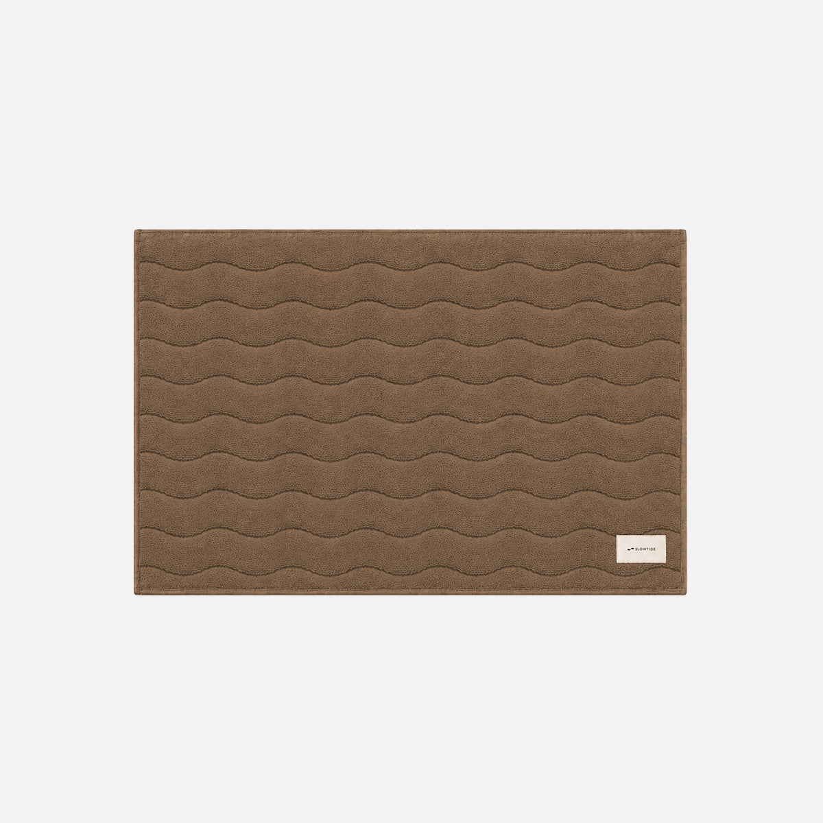 Cotton bath mat with wavy stitching and a small white label in the corner.