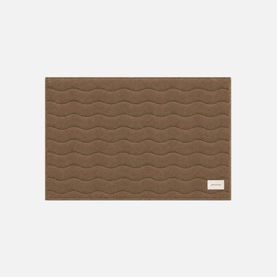 Cotton bath mat with wavy stitching and a small white label in the corner.