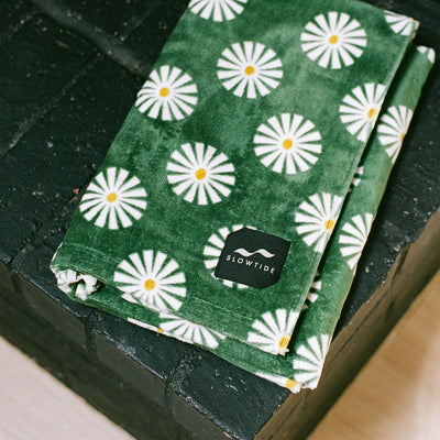 Green beach towel with white daisy pattern, folded on a dark brick surface.