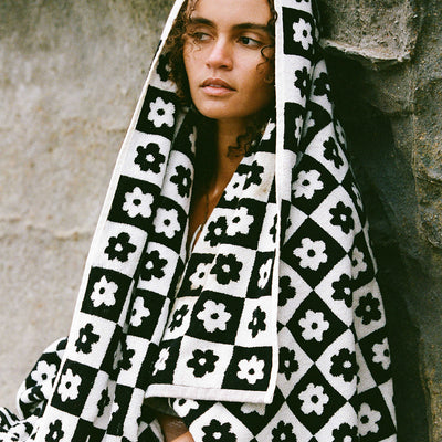 Bath towel with black and white floral pattern, draped over a stone wall.