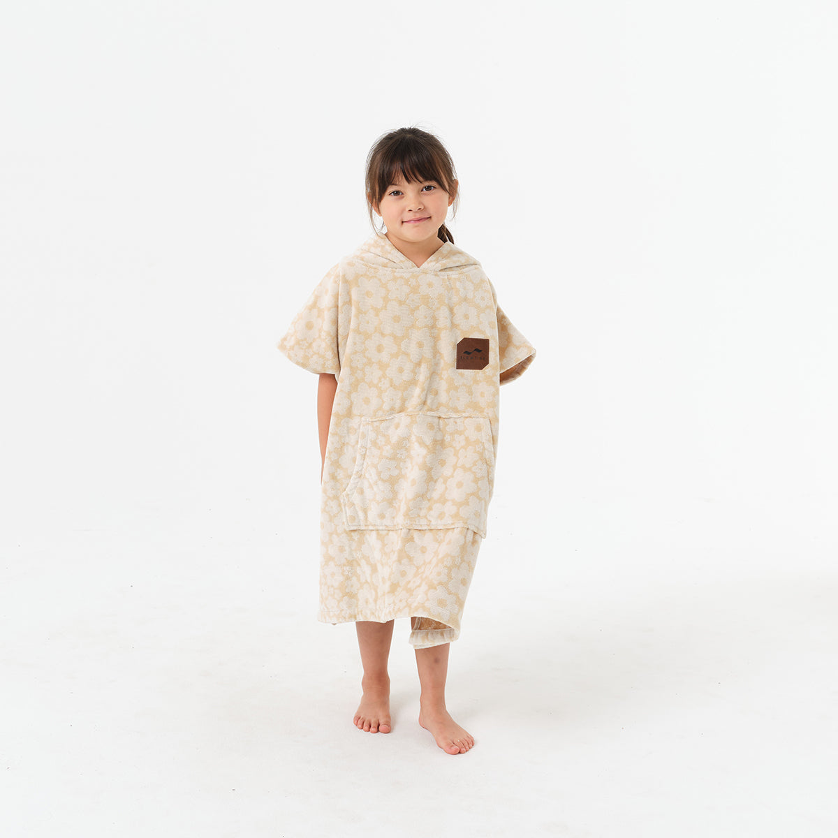 Kids’ cotton terry poncho in a tan flower pattern with a square chest patch.