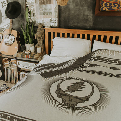 Blanket with skull and lightning bolt pattern on bed in cozy bedroom setting.