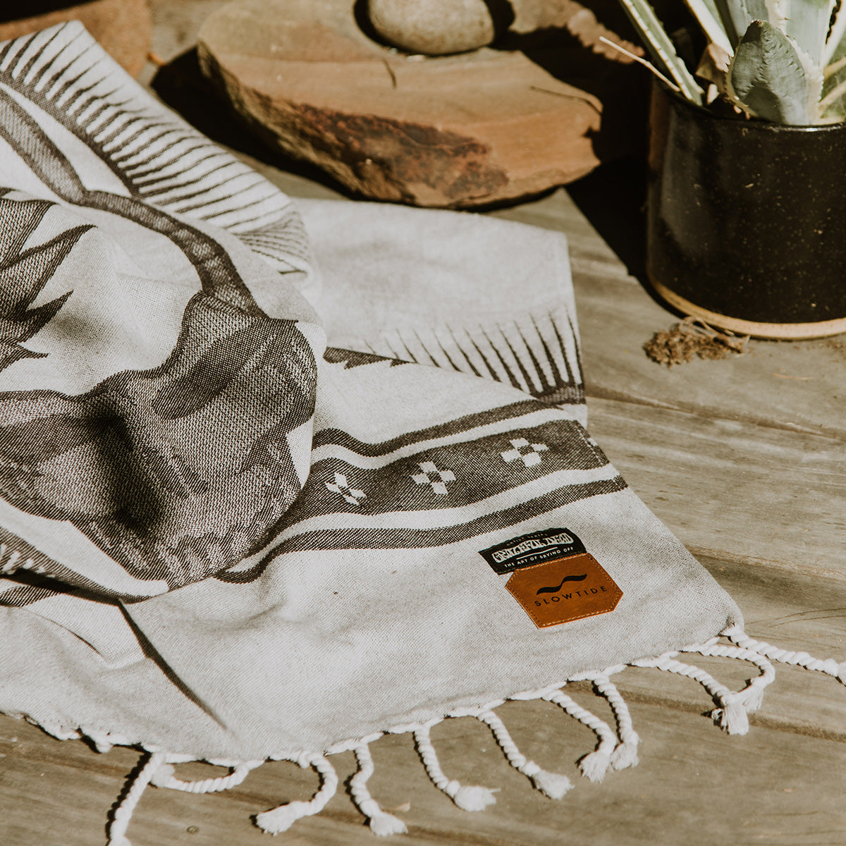 Picnic blanket with tassels and labels on a wooden surface.