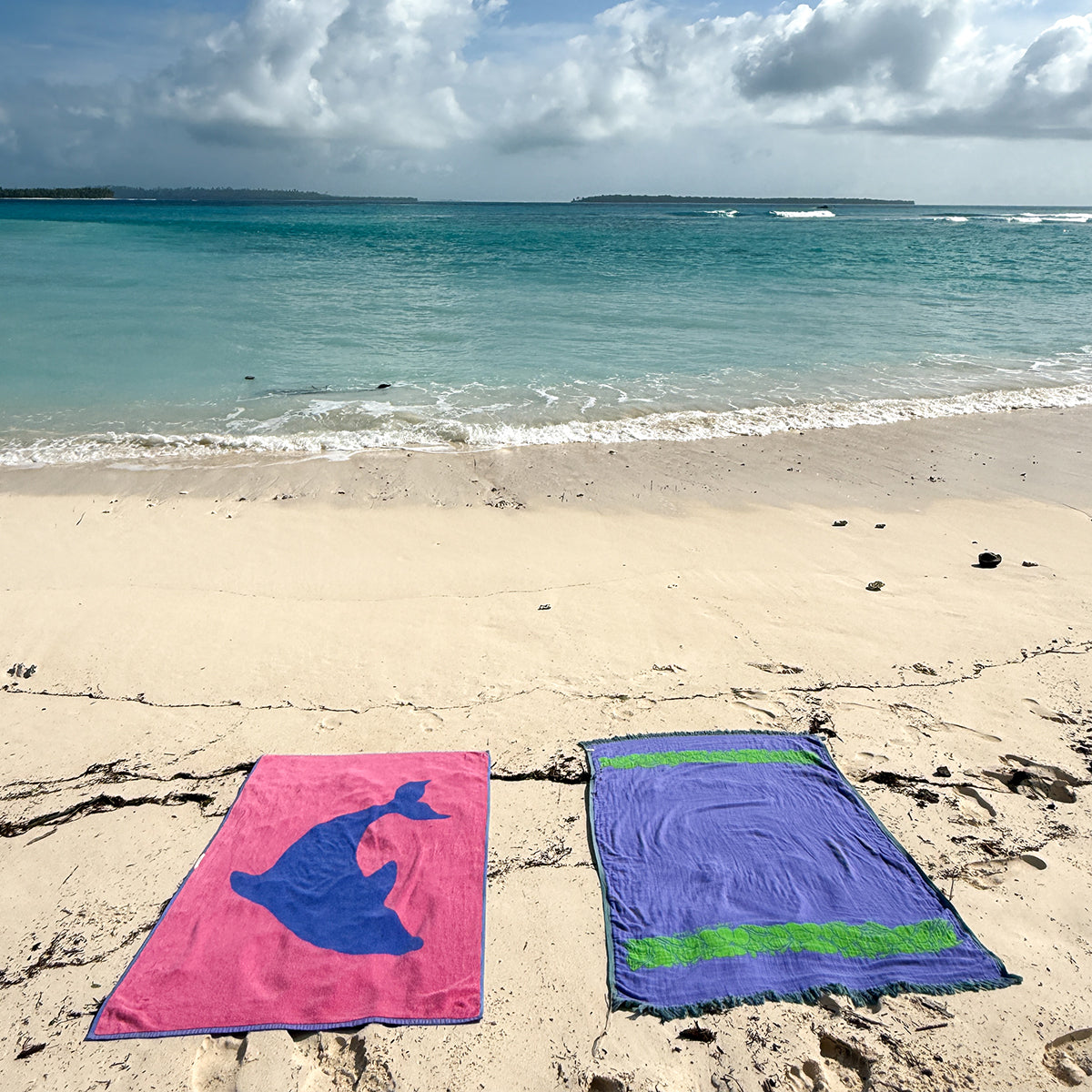 Beach towels, sand-resistant material, shown on beach near turquoise water.