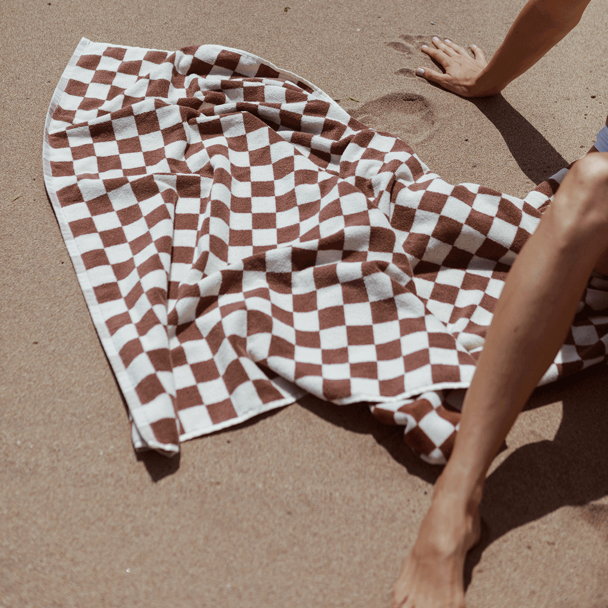 Jacquard beach towel, brown and white pattern, lying on sand.
