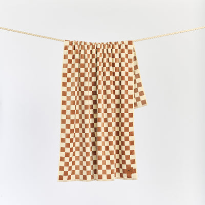 Beach towel, jacquard material, brown and cream checkered pattern, hanging on rope.