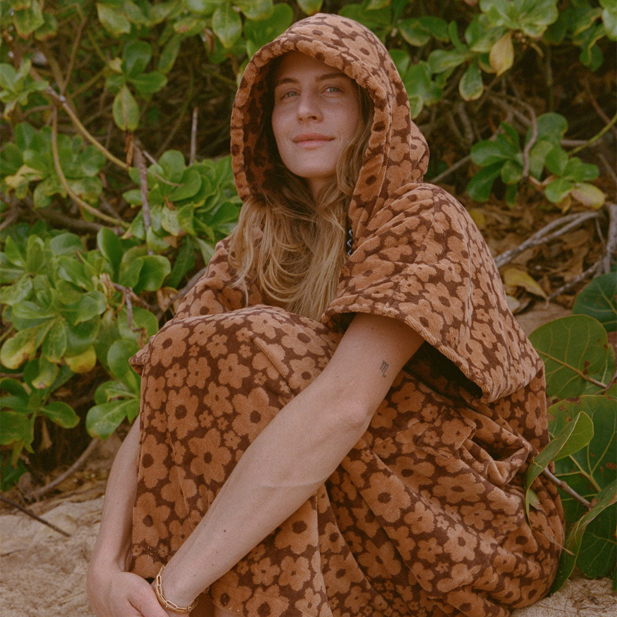 Brown floral cotton poncho with botanical print displayed near green plants.