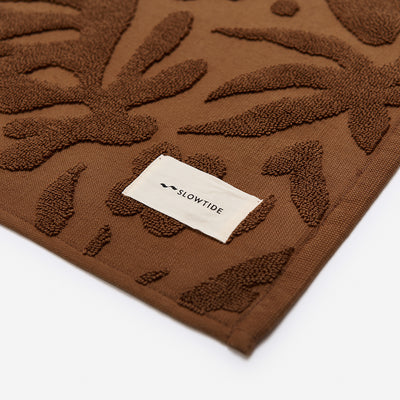 Brown cotton towel, plush and cushioned with white label detail.
