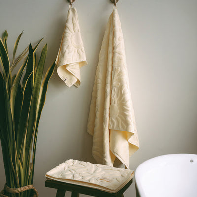 Pale yellow cotton bath towels with embossed sun pattern hanging on hooks.