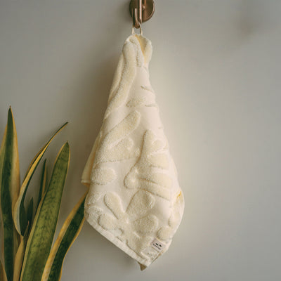Cream cotton hand towel with 550 GSM sculpted floral pattern hanging on a wall hook.