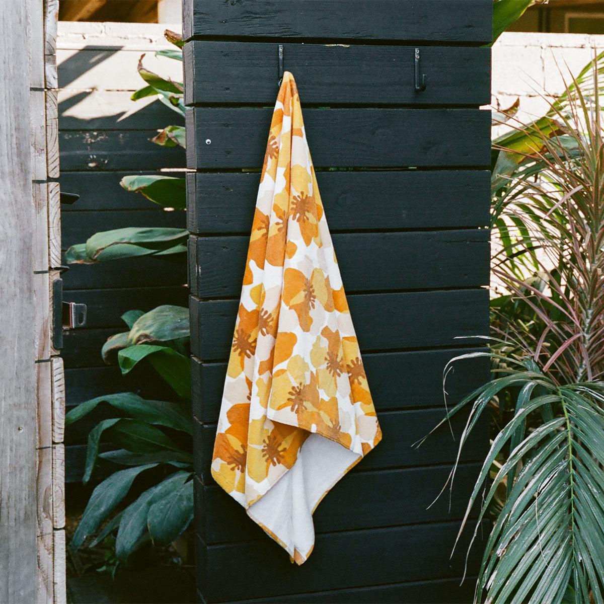 Yellow and white absorbent towel with striped pattern hanging on a black wooden fence.
