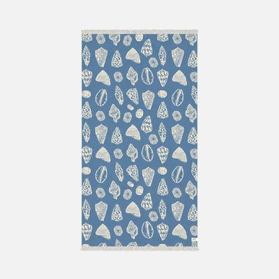 Blue cotton towel with white seashell pattern and fringe on short edges, top view.