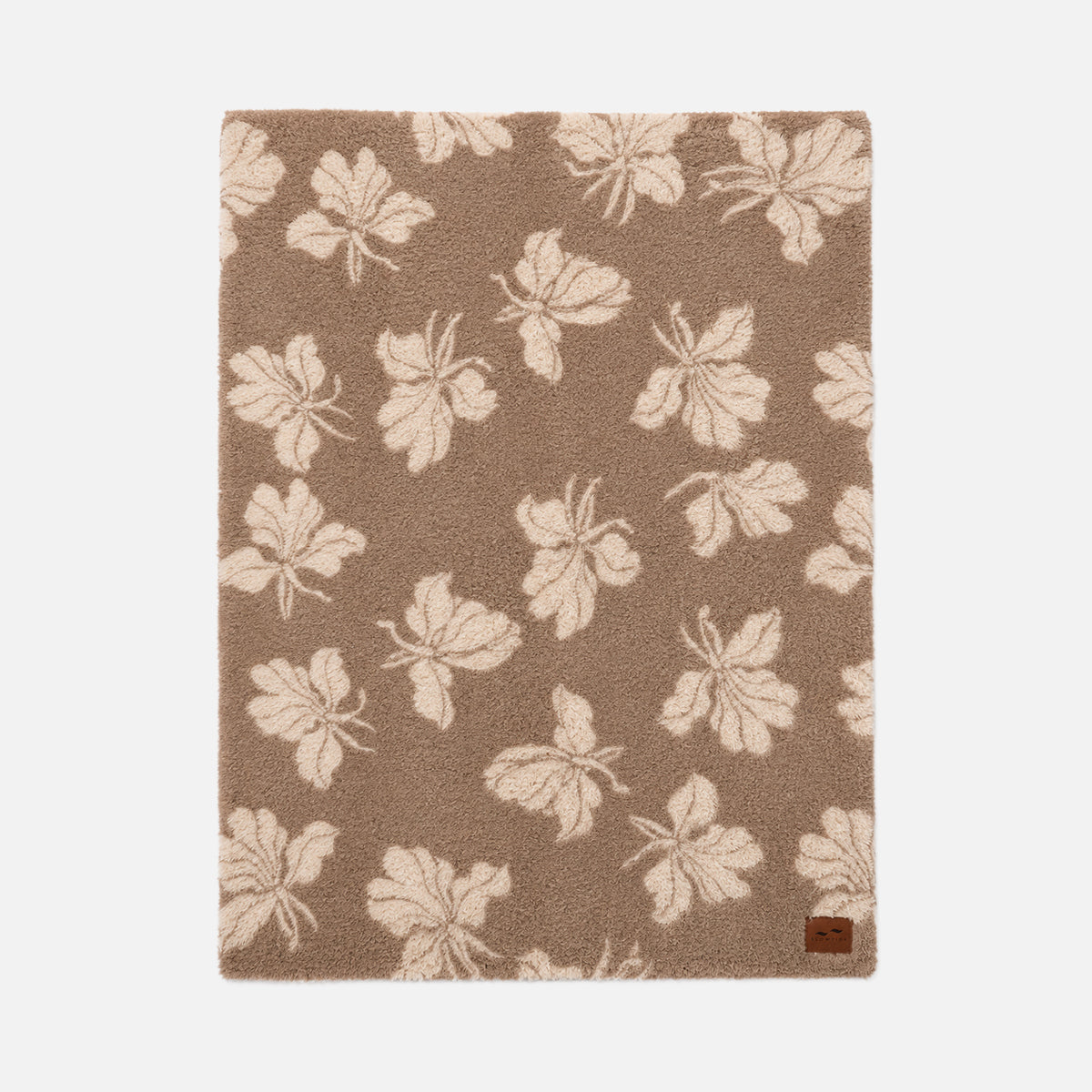 Tan area rug with cream leaf pattern, shown with a cozy throw for comfort.