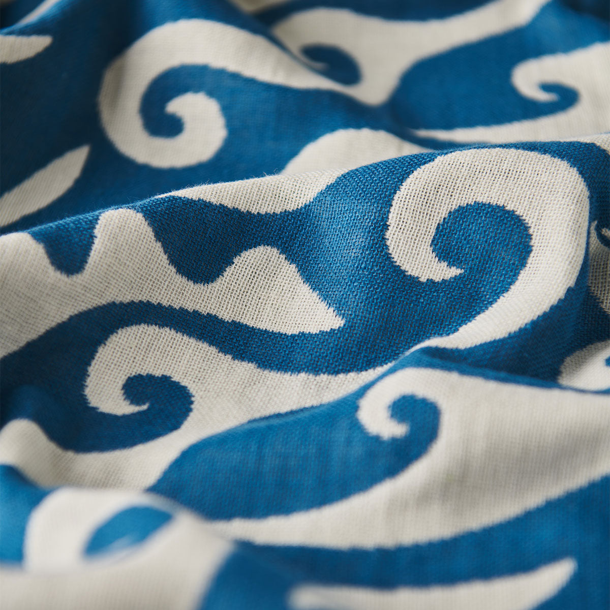 Fabric with ocean blue and white wavy swirl pattern, shown with light folds.