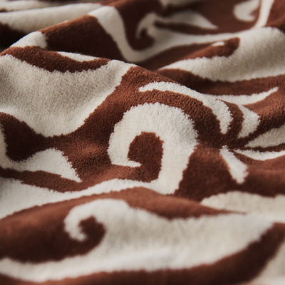 Fleece blanket with warm rust wave pattern on soft brown and white, vintage textile look.