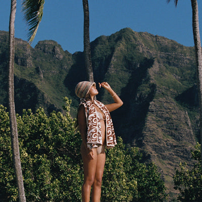Swimsuit with vintage textile pattern and straw hat, warm rust tones.