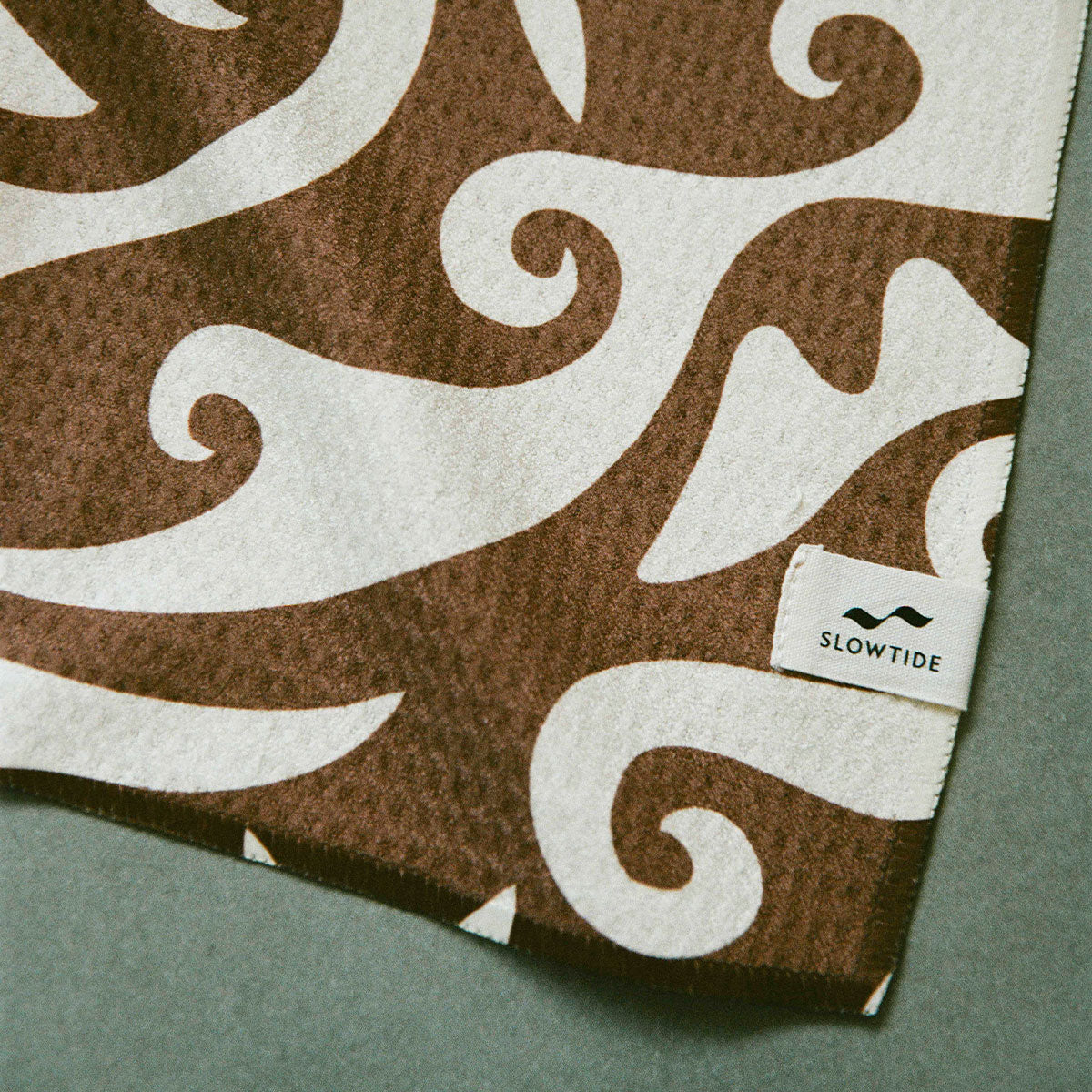 Sand resistant towel with brown and white pattern on gray surface.