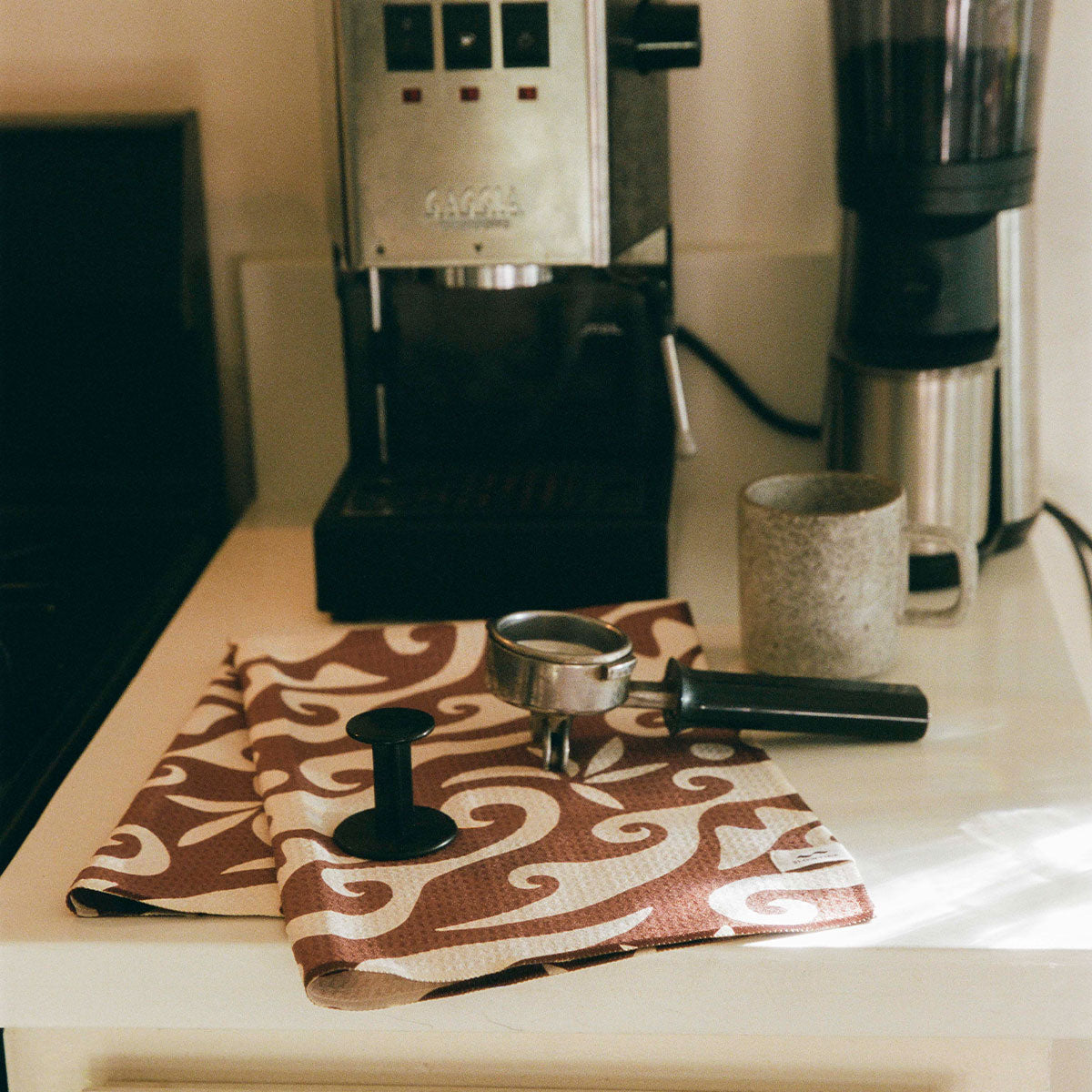 Espresso machine and grinder with portafilter, mug, and large towel on counter.