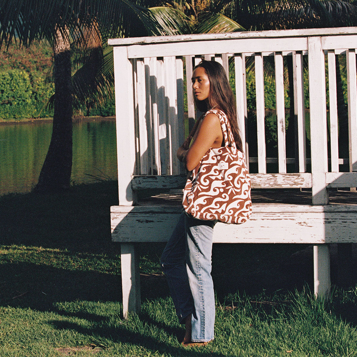 Patterned tote bag with built-in pocket on bench in outdoor light.