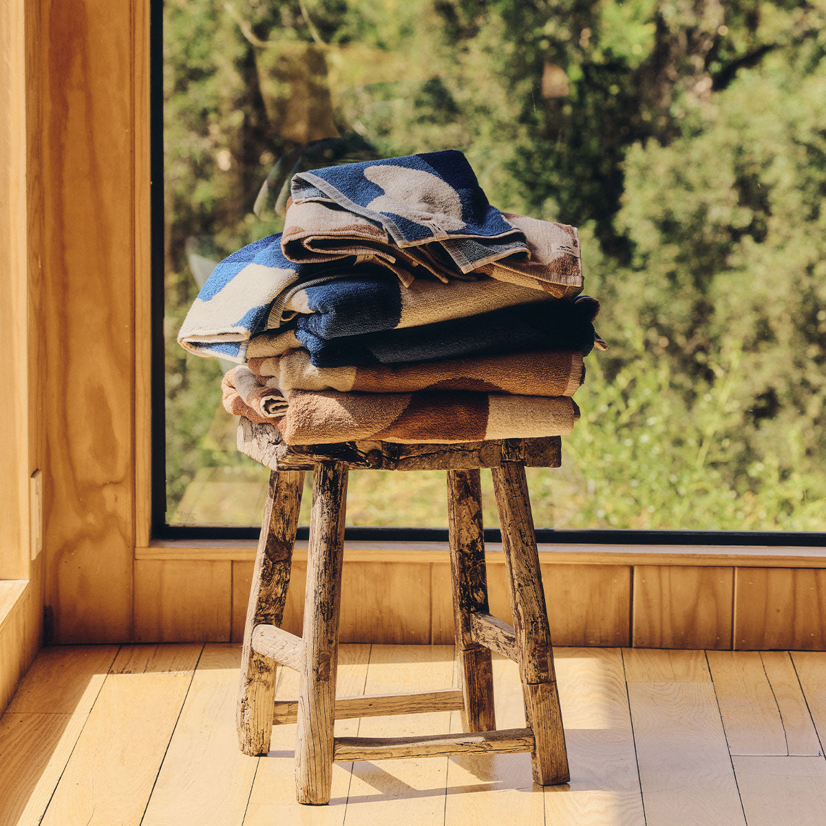 Patterned sand-resistant beach towels stacked on a wooden stool.