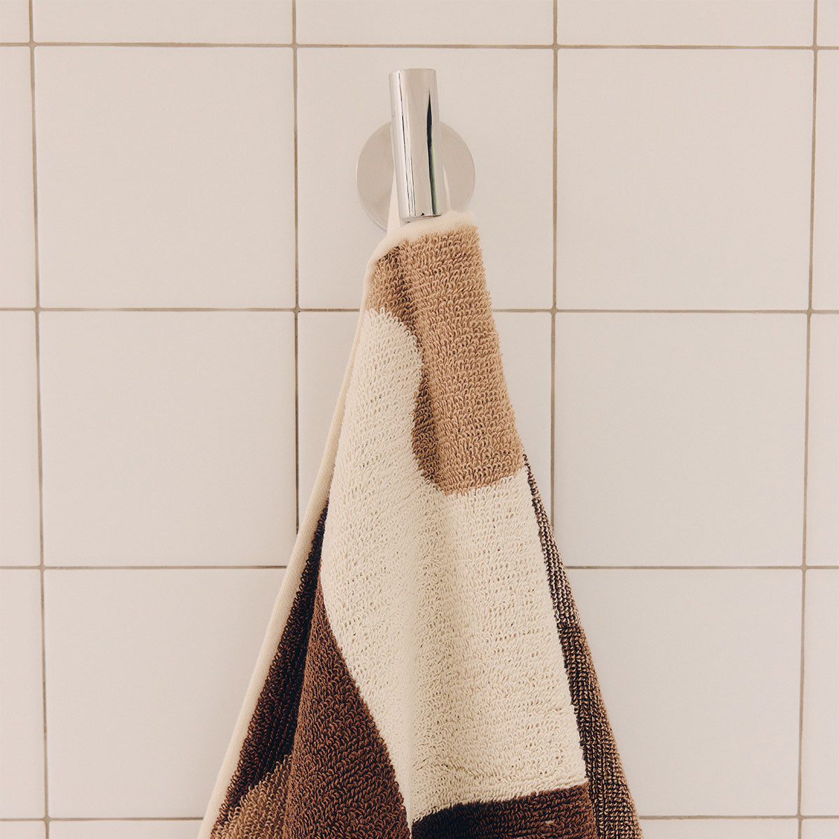 Cotton bath towel with brown and cream geometric pattern hanging on a hook.