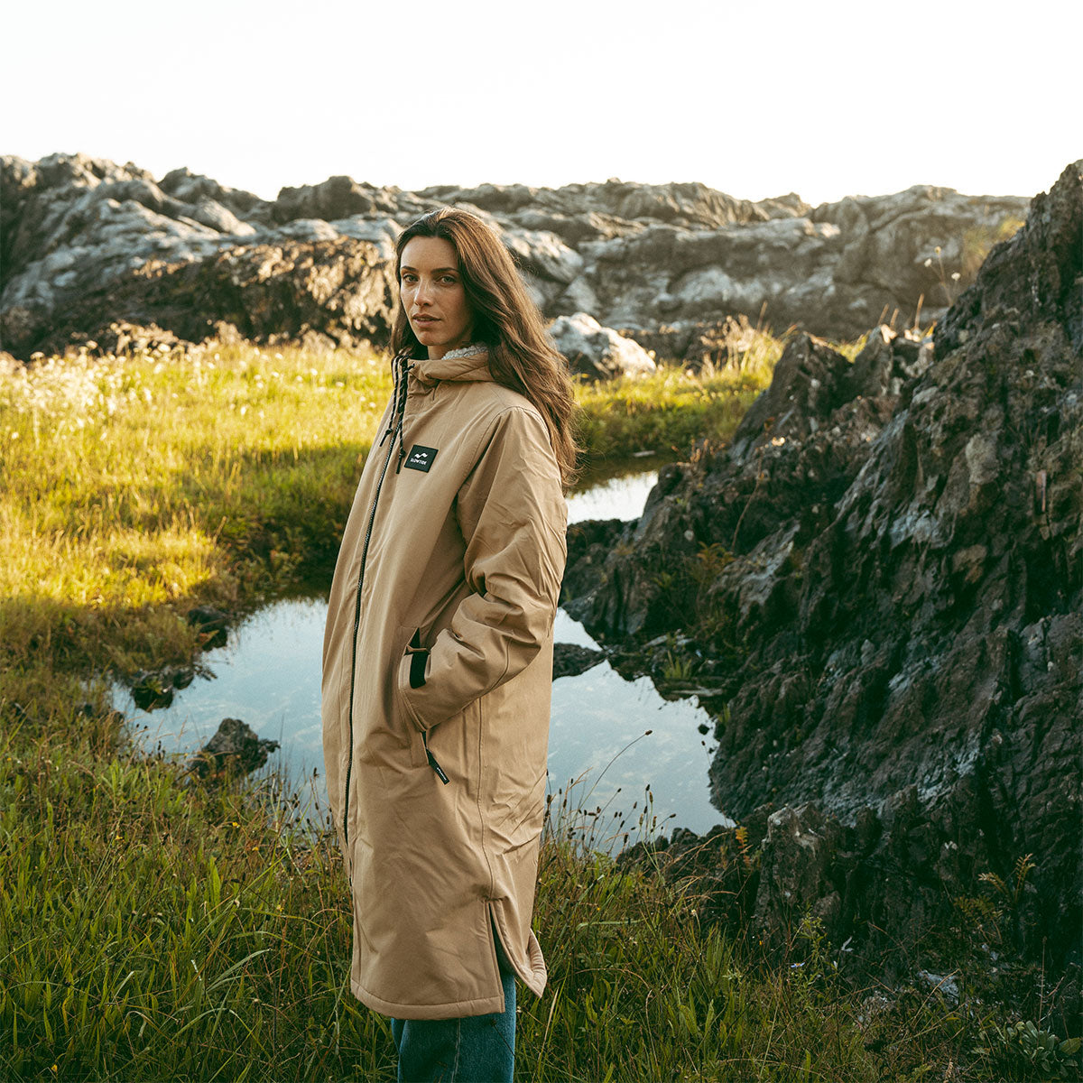 Tan all-weather parka with hood, outdoor setting.