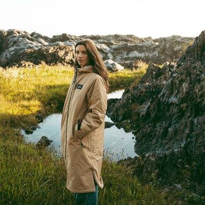Tan all-weather parka with hood, outdoor setting.