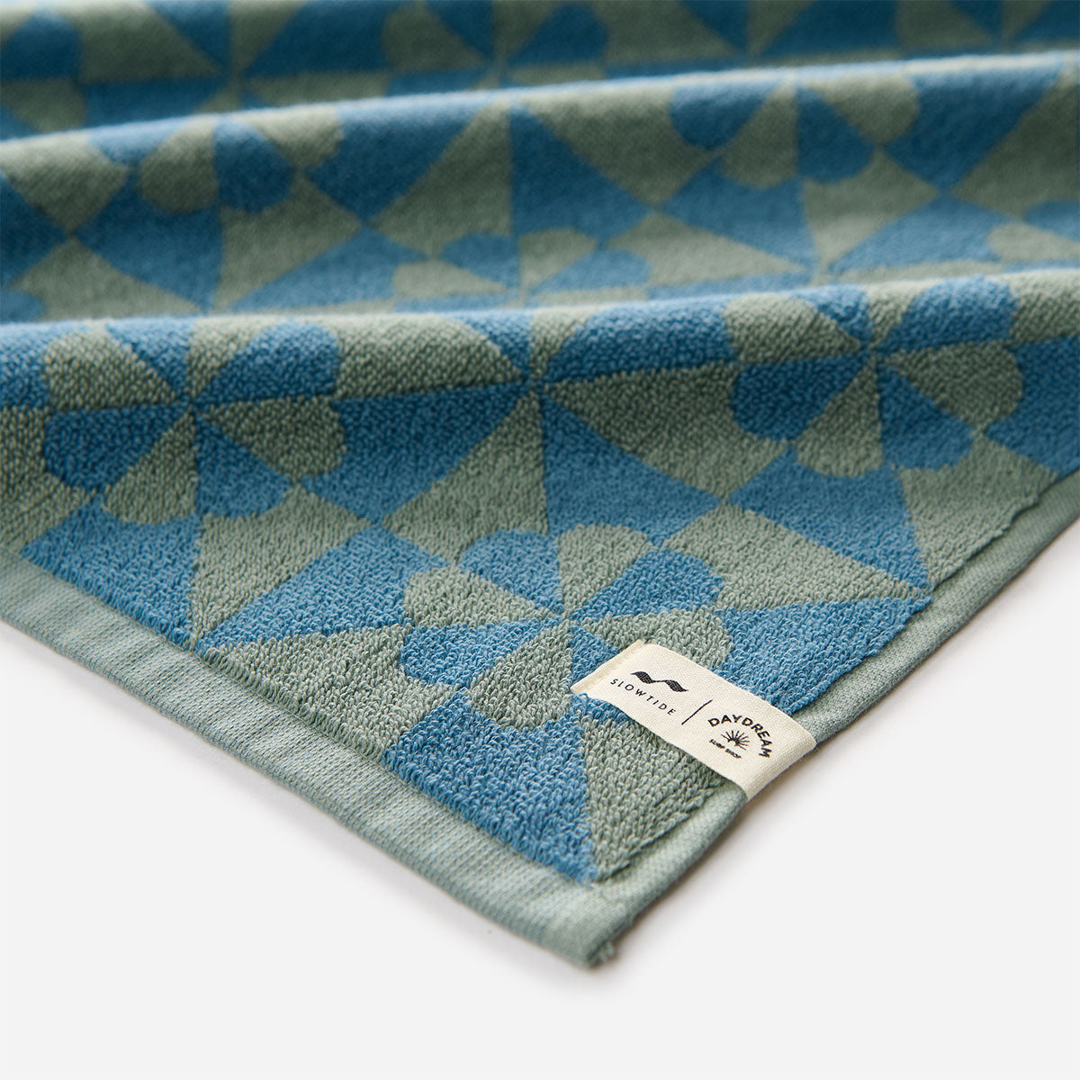Bathroom towel in blue and green geometric pattern with fabric label on edge.