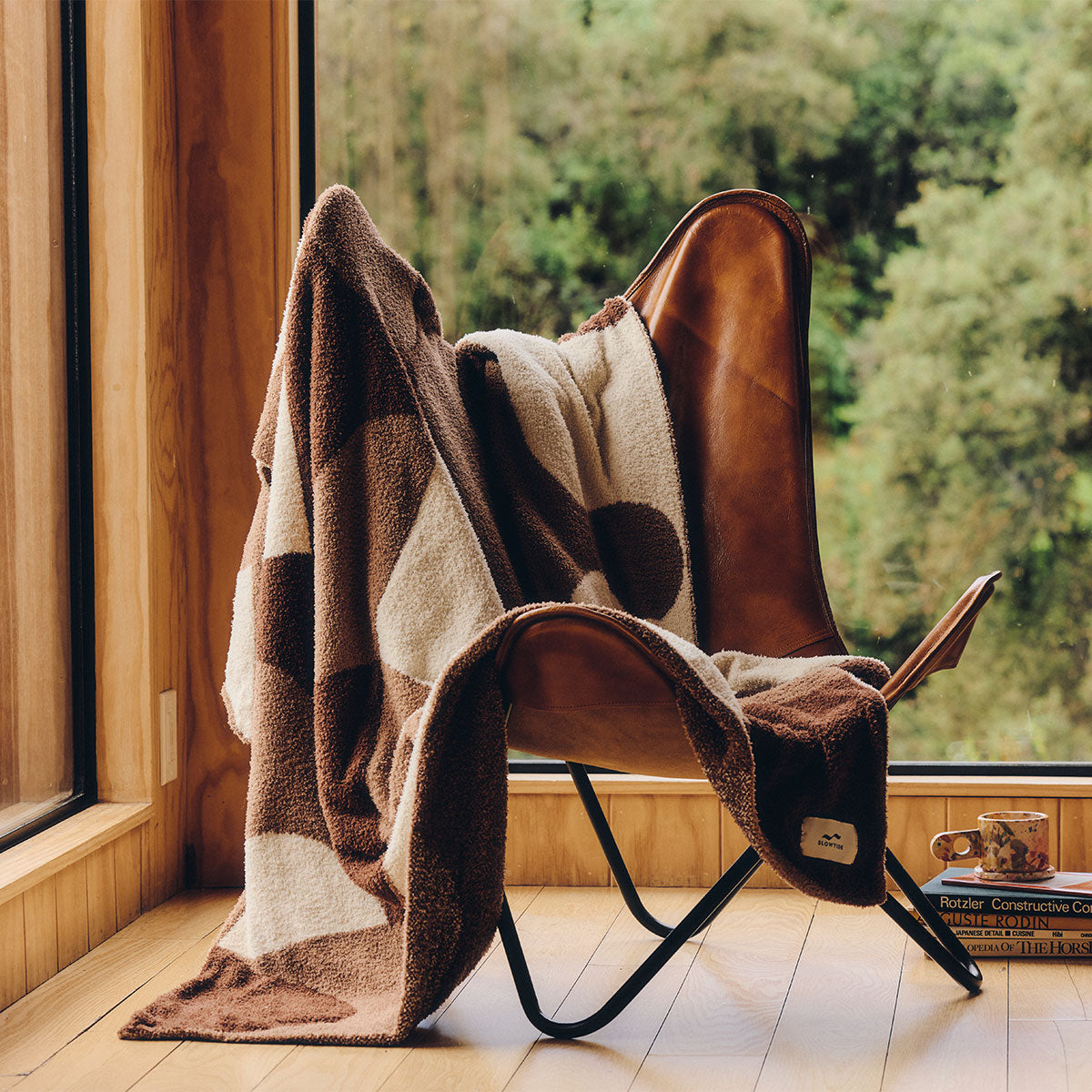 Plush knit blanket in brown and cream checkered pattern draped over a leather butterfly chair.