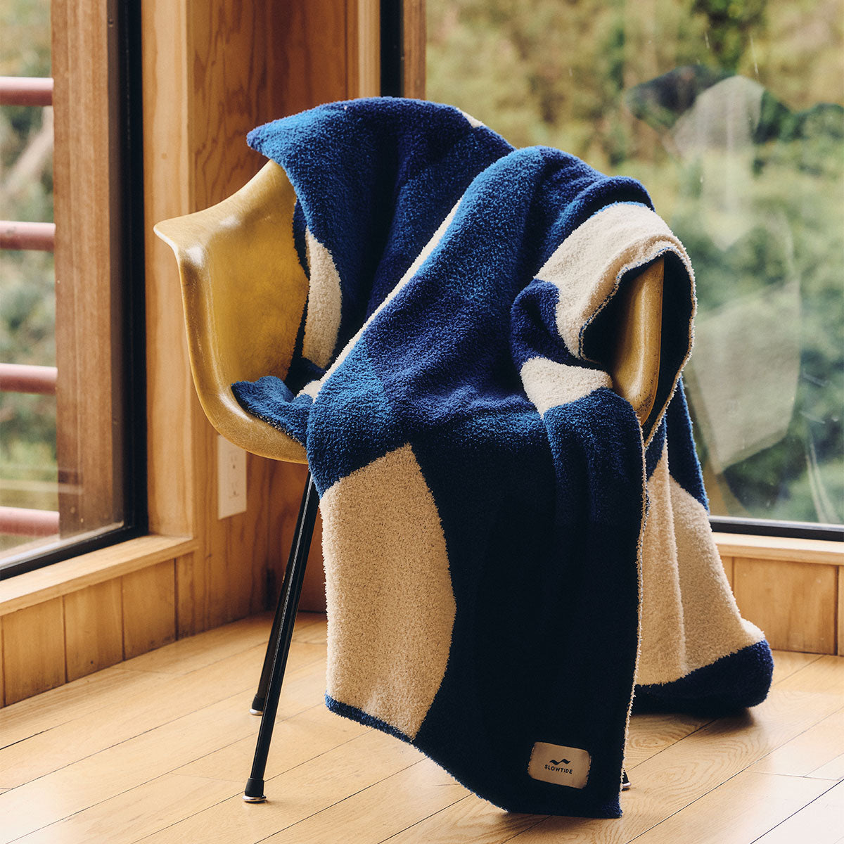 Plush knit throw blanket in blue and cream color-blocking draped over a chair.