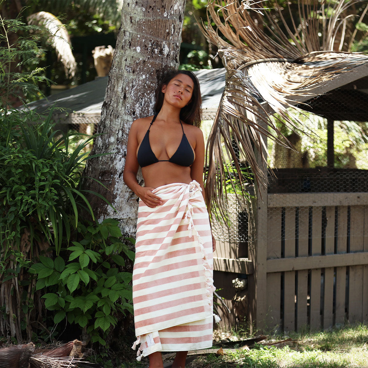 Black bikini top with striped sarong featuring tassel fringe in outdoor sunlight.