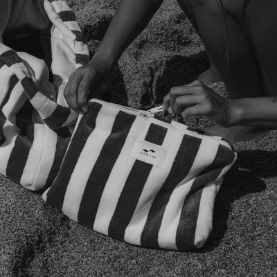 Striped terry pouch with matching towel detail on sand, poolside accessory.