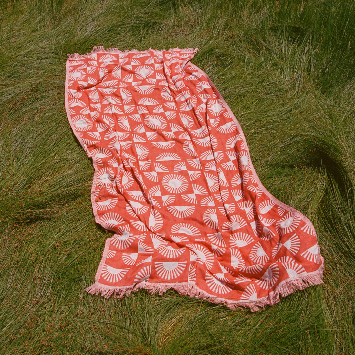 Turkish towel, lightweight red fabric with white fan pattern, on grass.