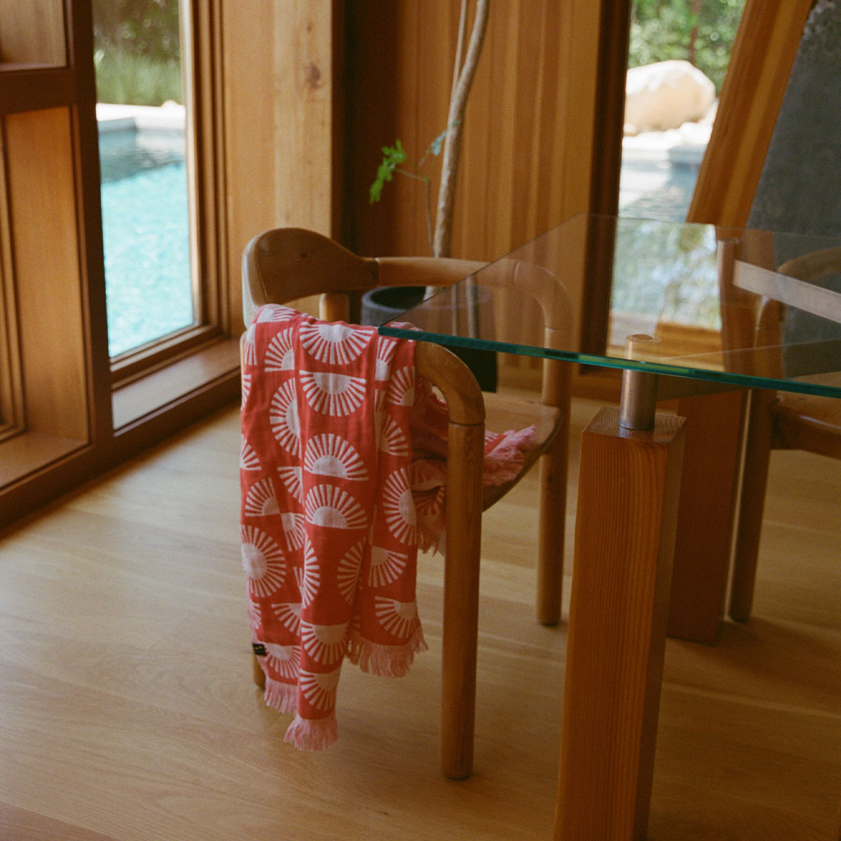 Turkish towel, cotton, red and white stripes, displayed on wooden chair by poolside.