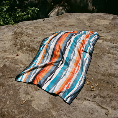 Quick-drying colorful beach towel with vibrant pattern displayed on a rock outdoors.