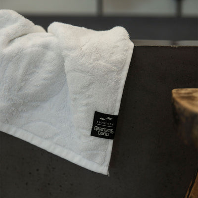 Towel with distinctive skull logo pattern draped over edge of dark bathtub.