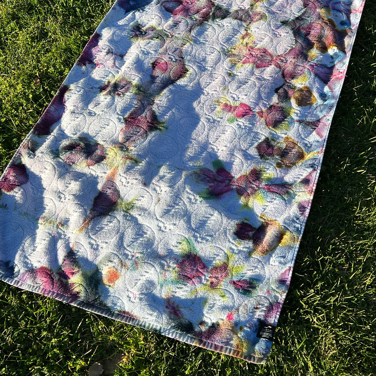 Bath towel with floral pattern on grass in sunlight.